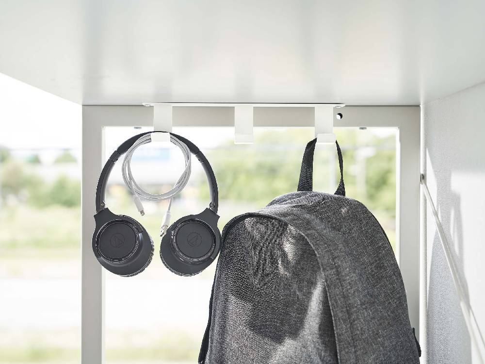 デスク下に取り付けられた銀色のスチール製タワーフック3連で、ヘッドセットや電気ケーブルが整理されている様子