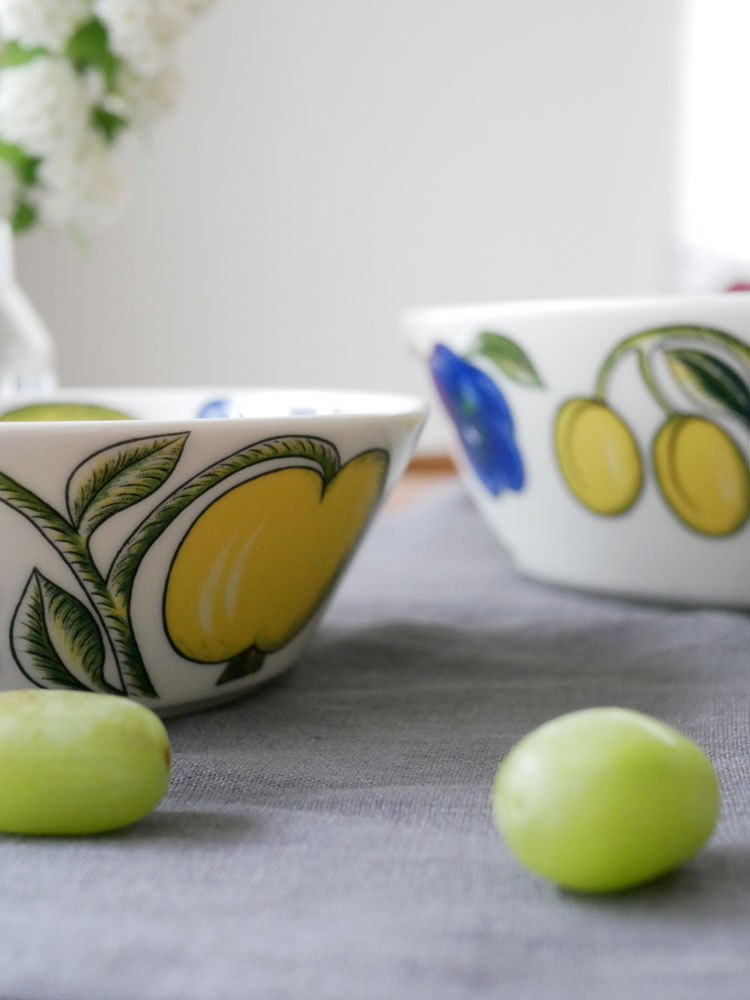 アラビア パラティッシ ボウルと果物、カトラリーが並んだ磁器製の食器セットがテーブルに配置されている様子