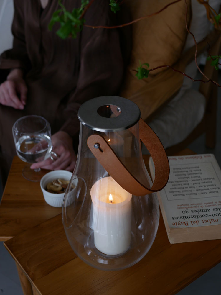 HOLMEGAARDのDESIGN WITH LIGHTランタン。無鉛ガラス、皮革、ステンレス鋼で作られ、キャンドルが灯された透明なランタン。
