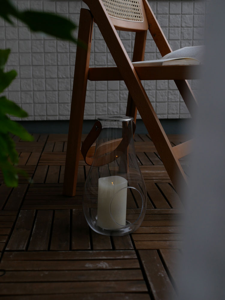 無鉛ガラスとステンレス製のホルムガードデザインランタンが木製家具と鉢植え植物と共に配置された屋外のシーン