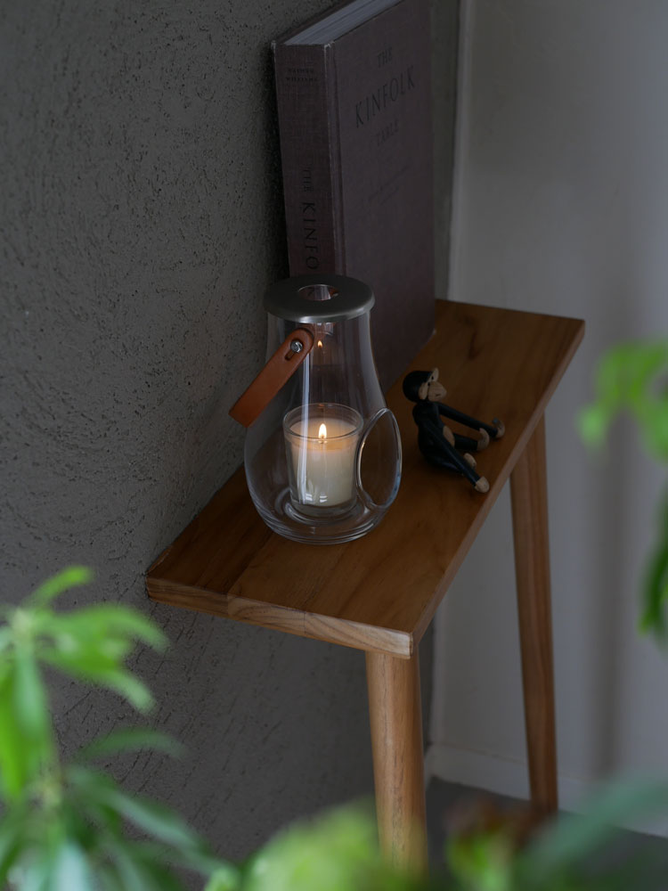 ホルムガードのDESIGN WITH LIGHTランタンが木目調のテーブル上に置かれ、観葉植物とガラス製の照明が配置されたスタイリッシュな静物写真