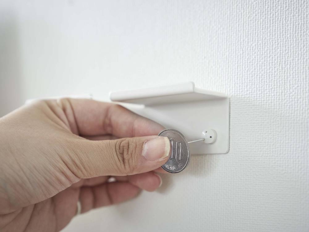 スチール製のタワー型ウォールスマートフォンホルダーが壁に取り付けられ、近くにAC電源ソケットとドアハンドルが配置されている様子