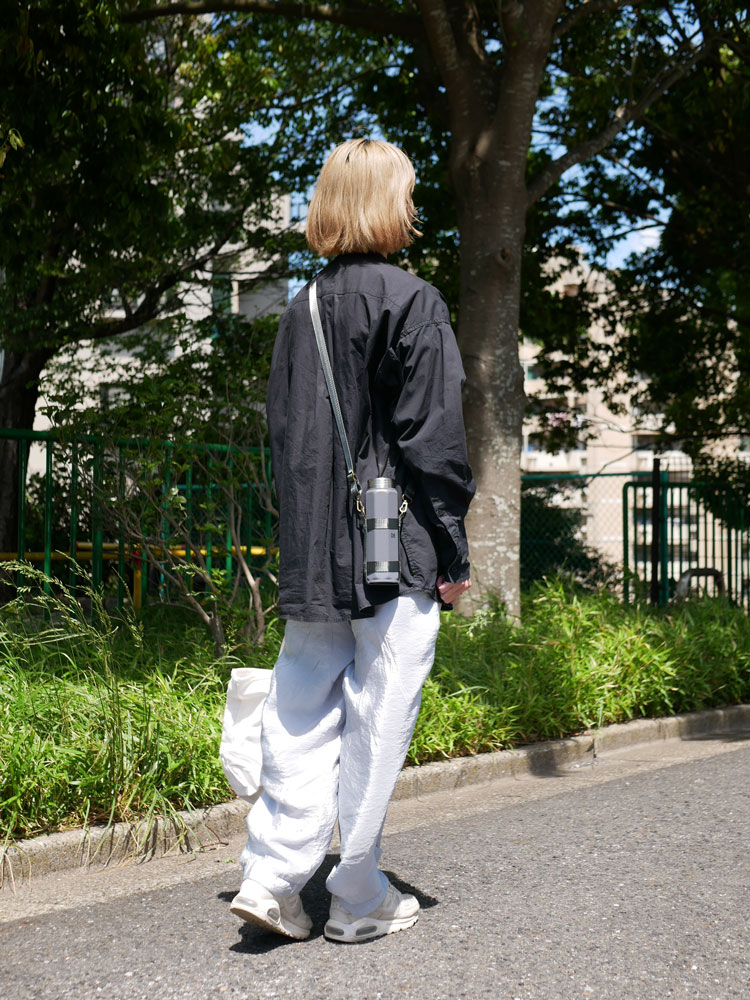 デニム製のCB JAPANホルムスオクタボトル ロングショルダーバッグを背負って歩くスタイリッシュな人物