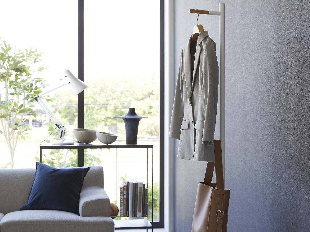 灰色のスチール製タワー型エントランスコートハンガーに木製フックが付いており、木材の床の上に設置されている様子。