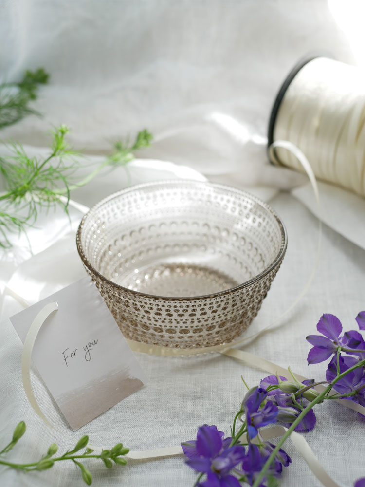 籐製の収納バスケットと銀色の食器の隣に置かれたイッタラのカステヘルミボウル