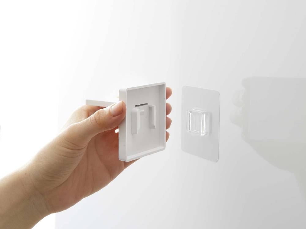 プラスチック製フィルムフックにマグネットタンブラーが掛けられた壁と近くのライトスイッチ