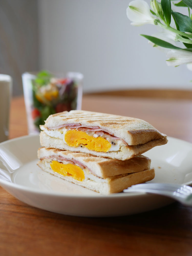 朝食用に指で食べられるエッグサンドイッチと食器がテーブルに並べられている様子