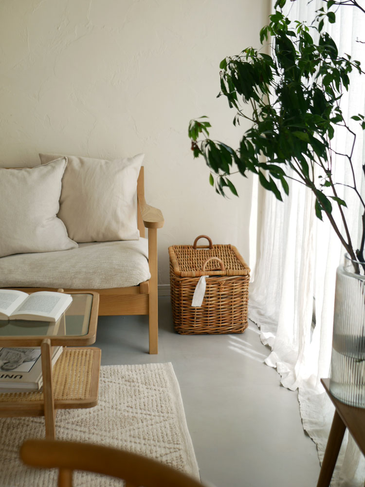 インドネシア製の皮つきラタンで作られたクレエの運べる収納バスケットが、木製フロアのリビングルームに配置され、観葉植物やクッションとともにナチュラルな雰囲気を演出しています
