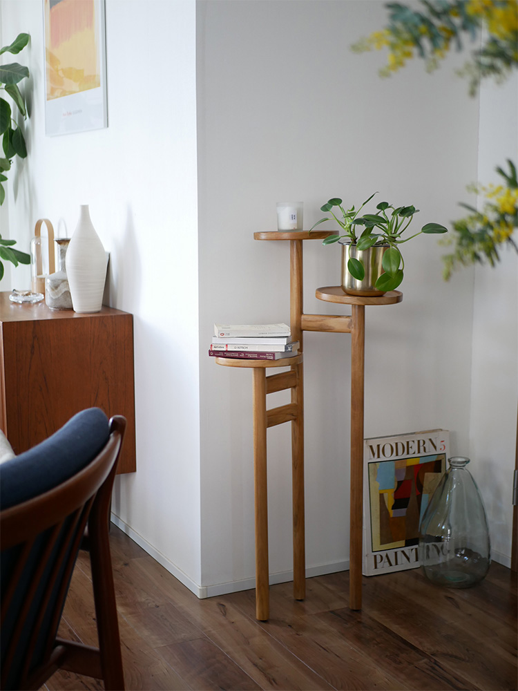 ナチュラルなチーク無垢材で作られたサンフラワーラタンステップトレイテーブル。複数の棚に花瓶や観葉植物が飾られています。