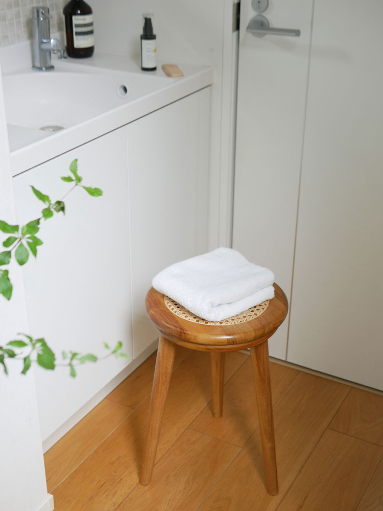 チーク材とラタン製のサンフラワーラタンスツールが木製のフローリング上に配置され、周囲に花鉢とハウスプラントが置かれている様子