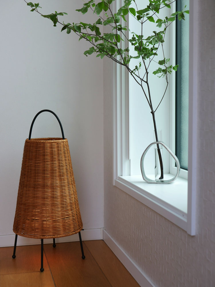 ハードウッド床にウィッカーバスケットとランプが配置され、【Creer/クレエ】サントリナアルミガラスベースの花瓶が飾られたナチュラルな室内