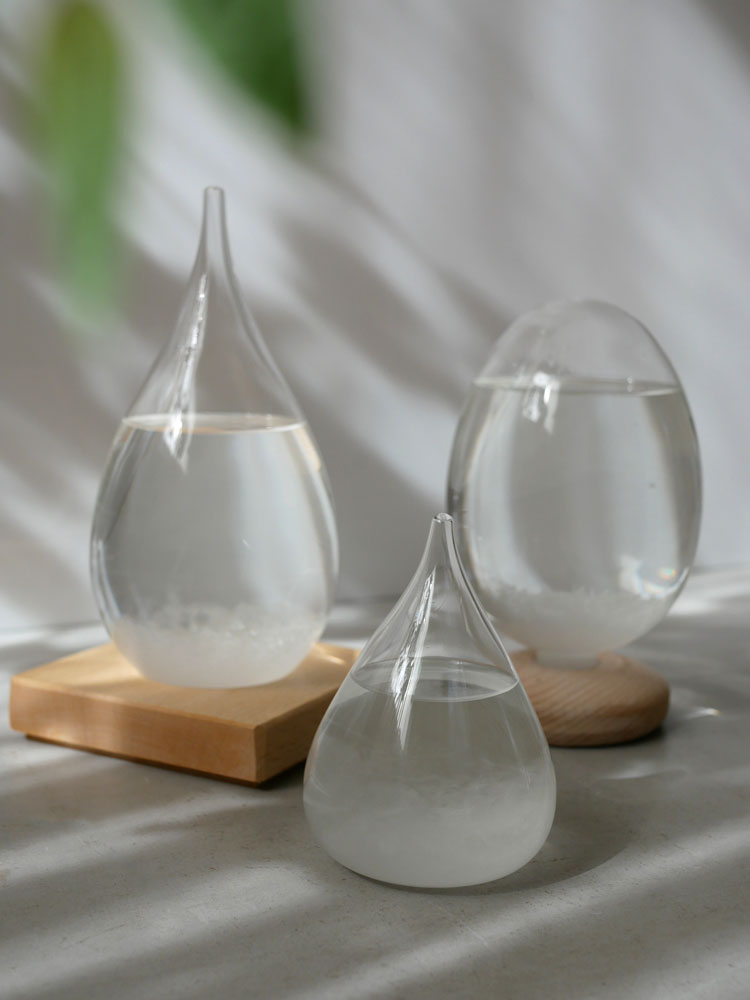 ヒャクパーセント製の透明ガラスボトル「Tempo Drop」が木製台座上に配置されたスタイリッシュな静物写真