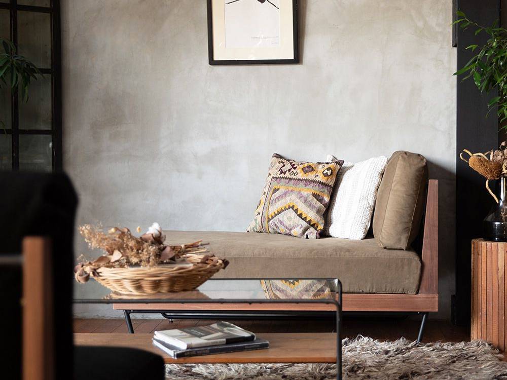 ウォルナットフレームのアデペシュウェルメカウチソファが、クッションとスローぴっくで彩られた居心地の良いリビングルームに配置されています。