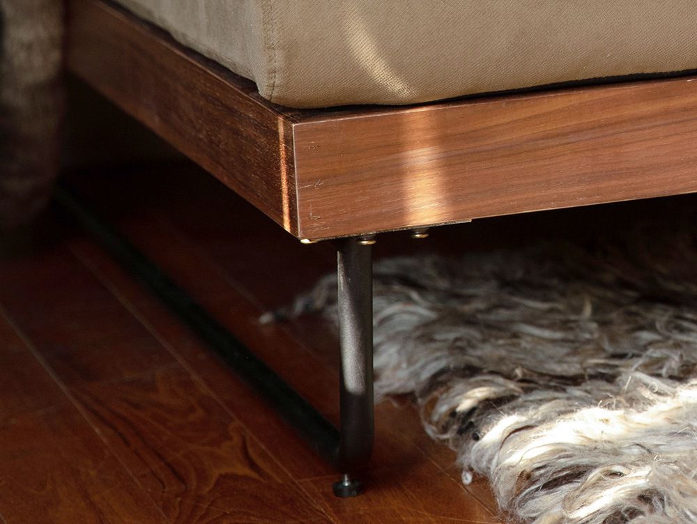 ウォルナット仕上げのウェルメカウチソファが、木製床とベッドフレームが配置された落ち着いたベッドルームのインテリア