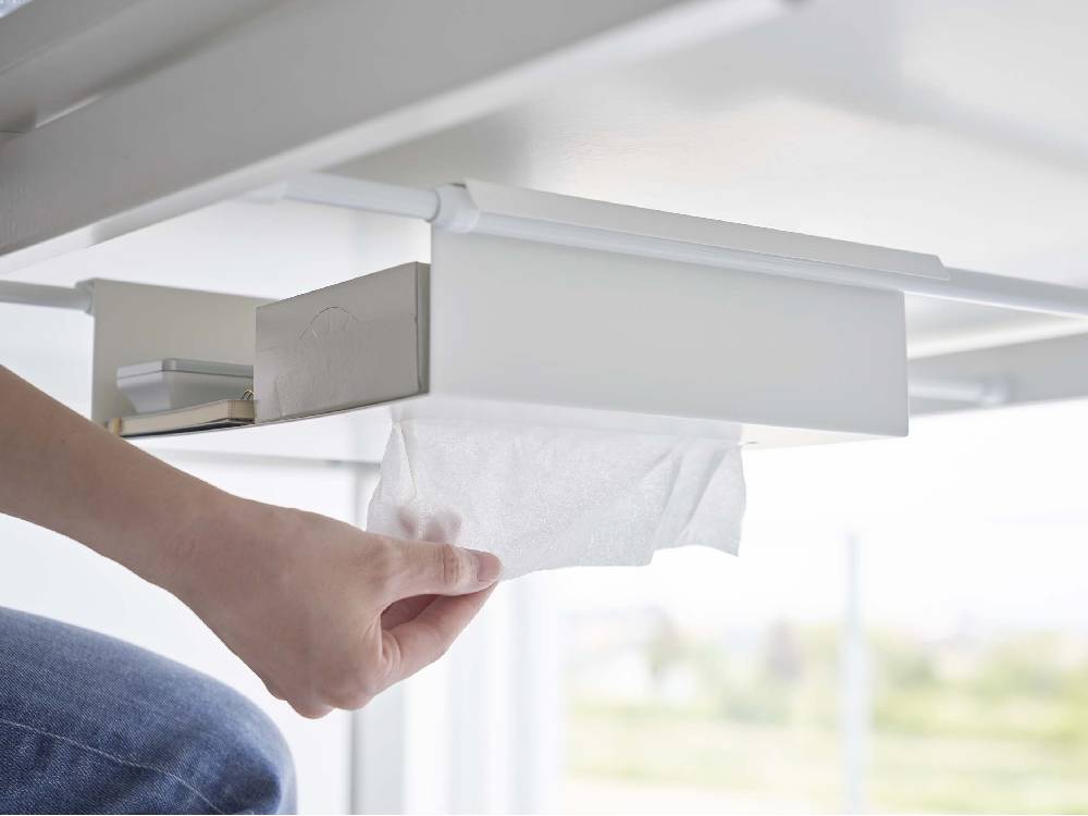 テーブル下に設置されたスチール製つっぱり棒用収納ラックに、ペーパータオルや事務用品が整然と並べられている様子