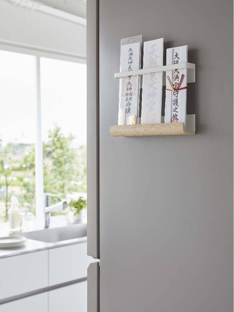 木製のキッチン棚に設置された【RIN/リン】マグネット神札ホルダー。観葉植物や家庭用品とともに整然と並べられた収納スペースの一部です。