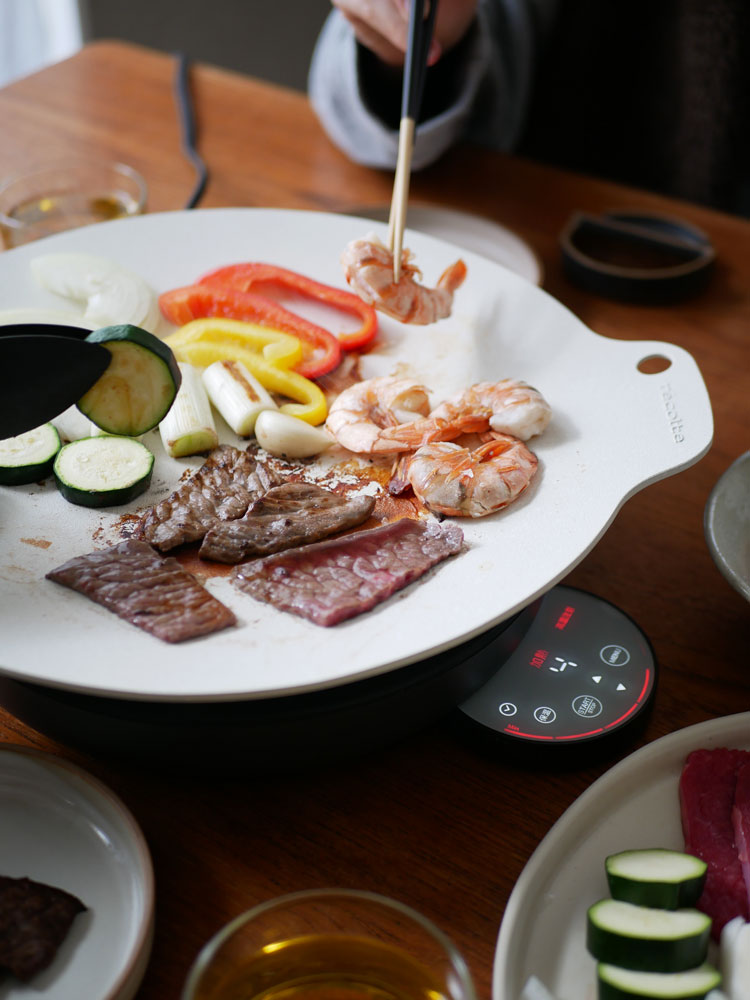 レコルトの卓上IHクッキンググリドル上で肉や野菜が調理され、テーブルウェアに盛り付けられている様子