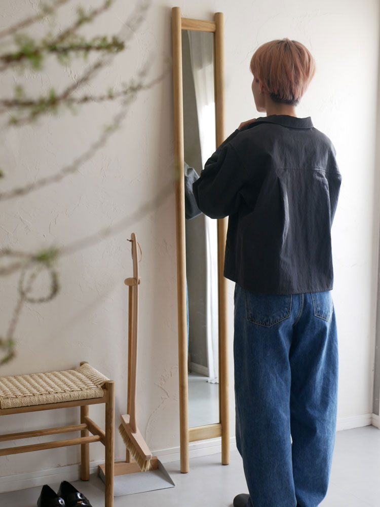 チーク無垢材とラタンを使用したHOKOS全身映るスリムミラーが木製フローリング上に置かれている