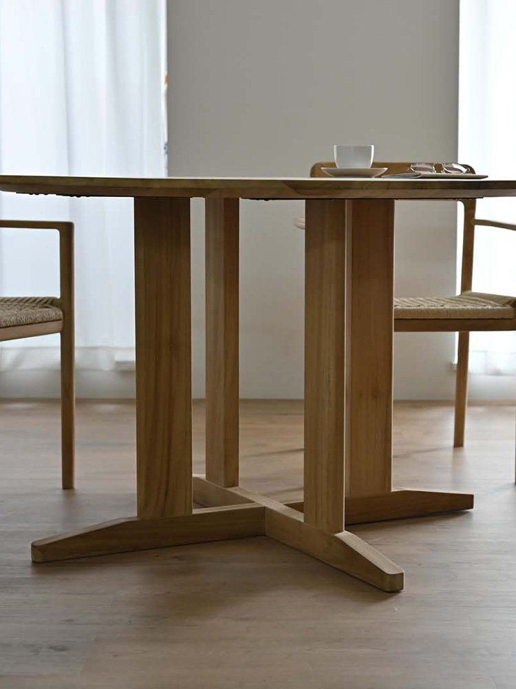 チーク無垢材製のHOKOSサンフラワーラタンラウンドダイニングテーブルが木製の床に配置されている様子