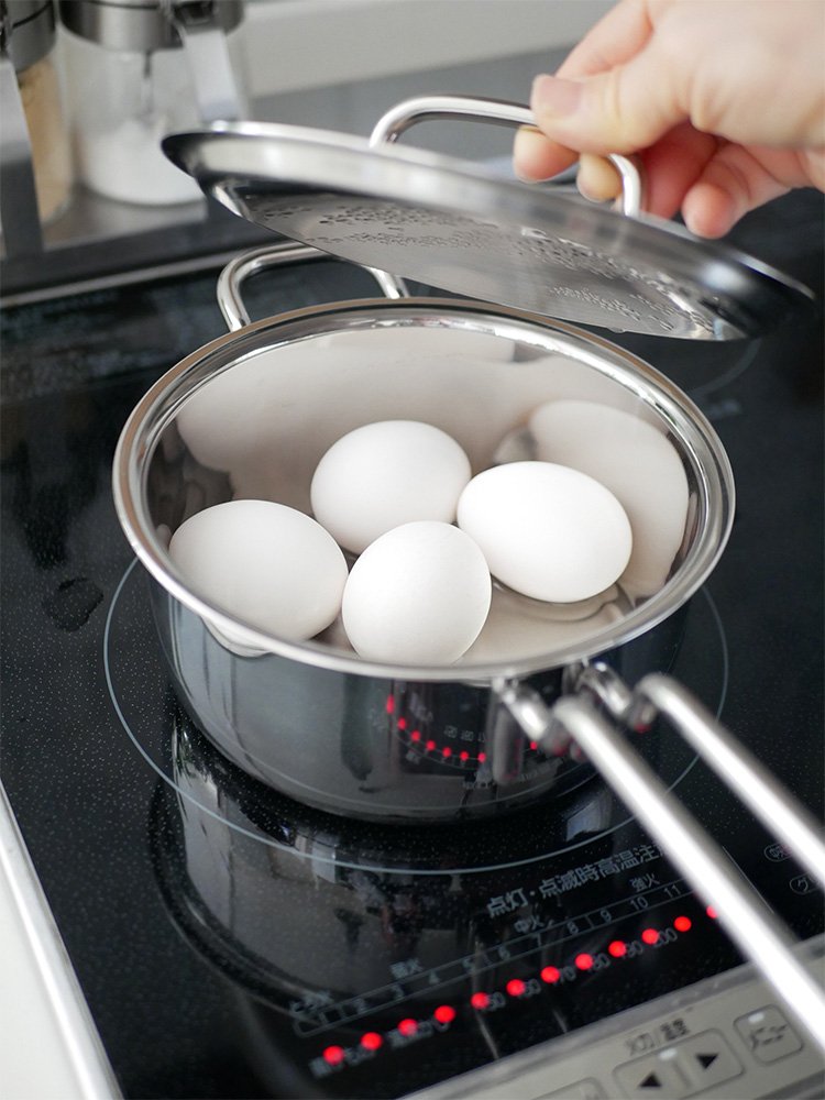 キッチンに配置されたジオプロダクトの15年保証日本製フタ付き鍋と調理器具、食材や卵が並んでいる様子