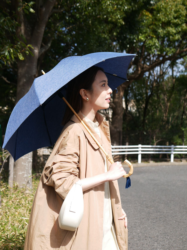 ビコーズのプレーンカラー傘を持ち、オーバーコートとバッグを着用したモデルがファッション撮影中の様子