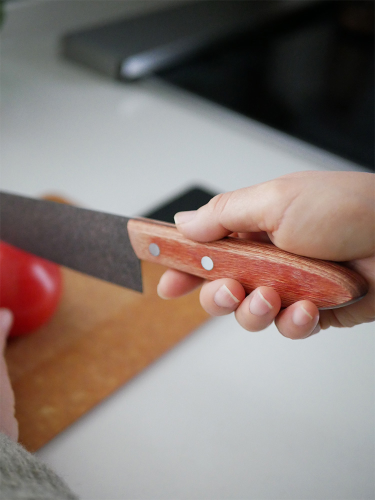 スーパーストーンバリア包丁と専用シャープナーが木製まな板上に配置され、フルーツや調理器具とともにキッチンで使用されている様子