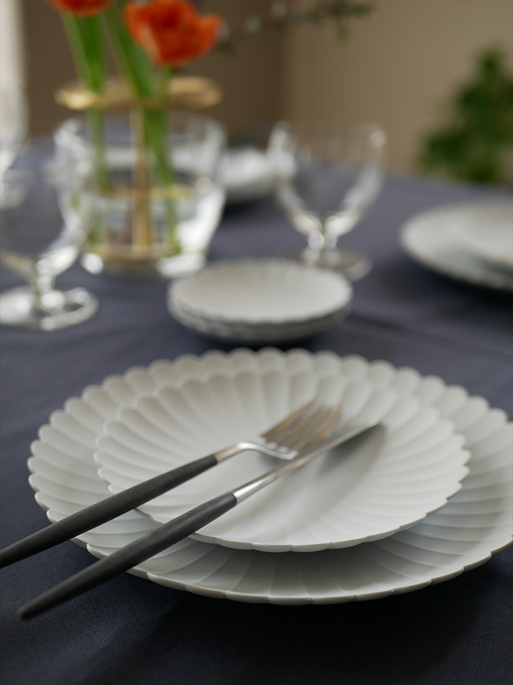 Cutipol/クチポールのMIOカトラリーセットとプレートがテーブルクロスの上に美しく配置されたディナーセッティングの画像