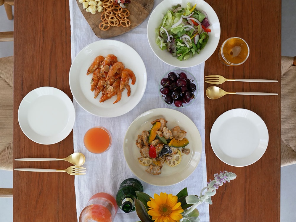 クチポールのMIOカトラリーセットと食器がテーブルに美しくセットされ、ブラックとアイボリーゴールドのフォーク、スプーン、ナイフが整然と並び、野菜やお皿が配置されている様子