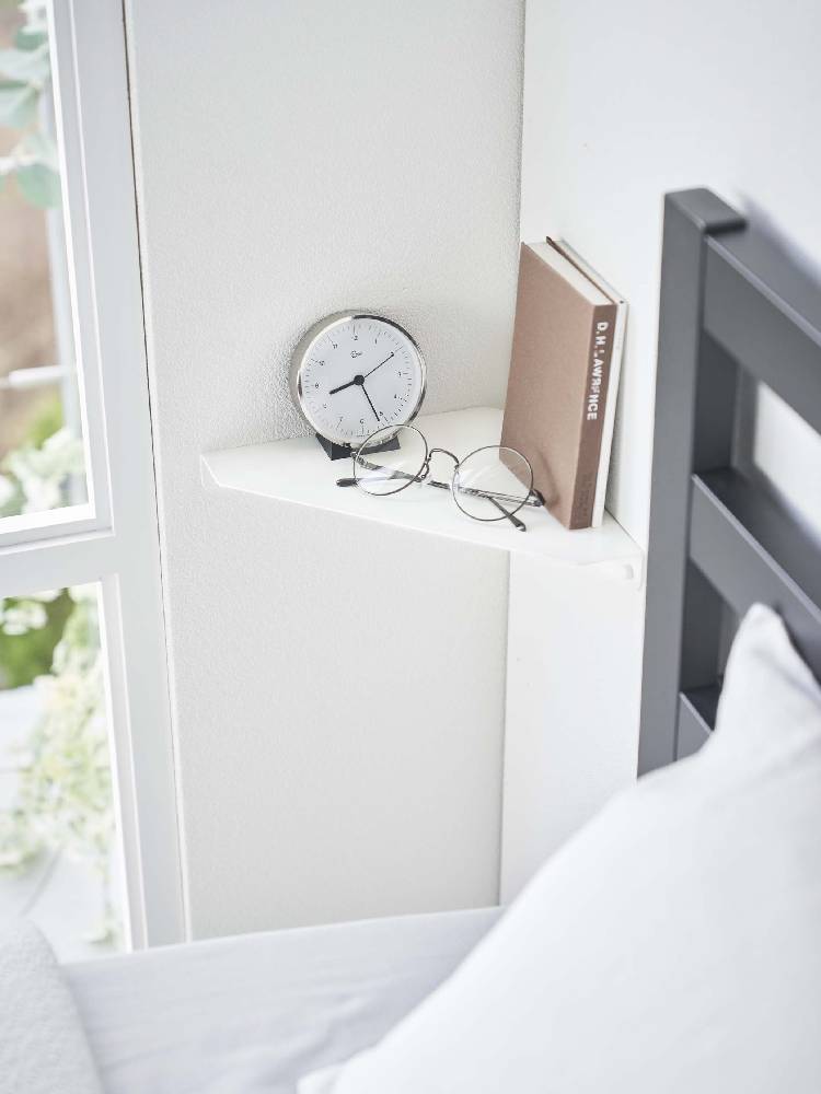 スチール製の石こうボード対応コーナーシェルフが配置されたベッドルーム。ベッド、ナイトスタンド、ランプ、クッションなどの家具が見える