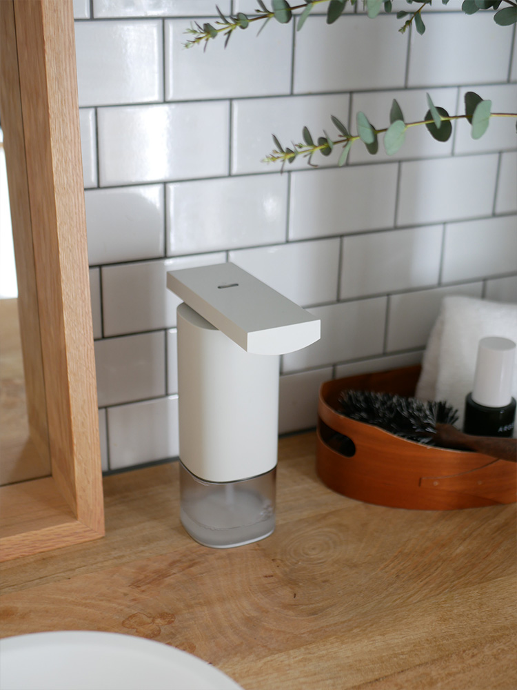 バスルームの洗面台に設置されたセラミック製オートソープディスペンサーと蛇口、観葉植物が調和したシーン