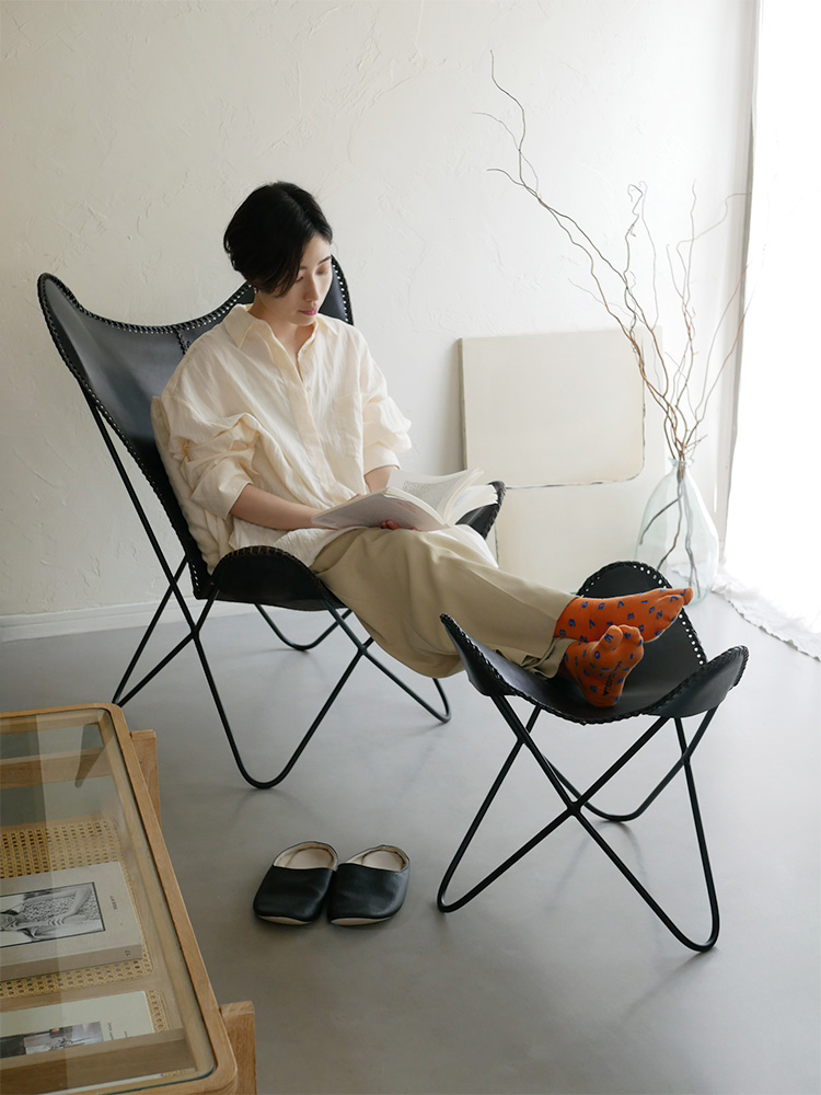 ラップスのアイアンレザースツールが木製フローリングのリビングルームに配置され、快適な座り心地とアームレストが特徴です。