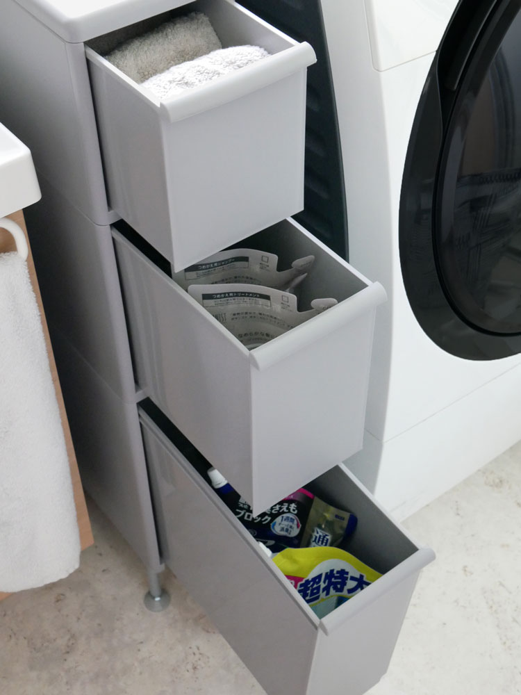 洗濯機と衣類乾燥機の隣に配置されたグレーのアジャスター付きスリムストッカーが整然と並ぶ洗濯室の棚