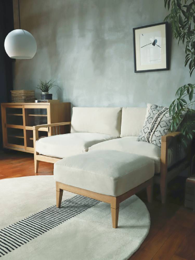 木製フローリングのリビングルームに配置されたアデペシュのsoloソファーとオットマン、カラフルなクッションがアクセントとなったインテリア