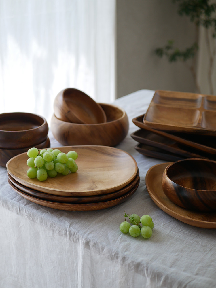 選べるやさしいアカシア食器セットがテーブルに並べられ、エッグ型トレーやスクエアトレー、ラウンドボールと共に果物や料理が盛られています。