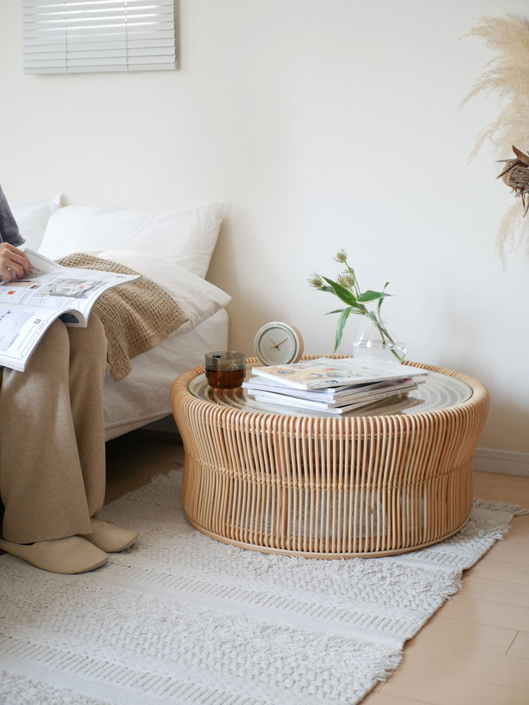 ラタンとガラス素材のサンフラワーラタンローテーブルがリビングルームの木製床に配置されています。