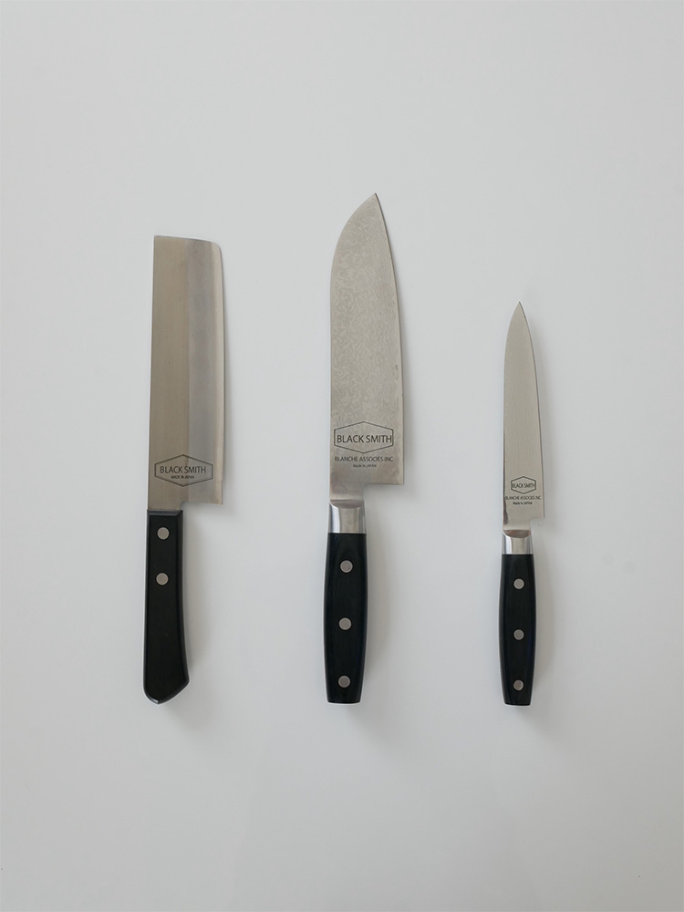 TOOLS/ツールズ ブラックスミス ナイフシリーズのダマスカス鋼製ナイフ（大型、ペティ、菜切り）が木製の背景に整然と並べられている