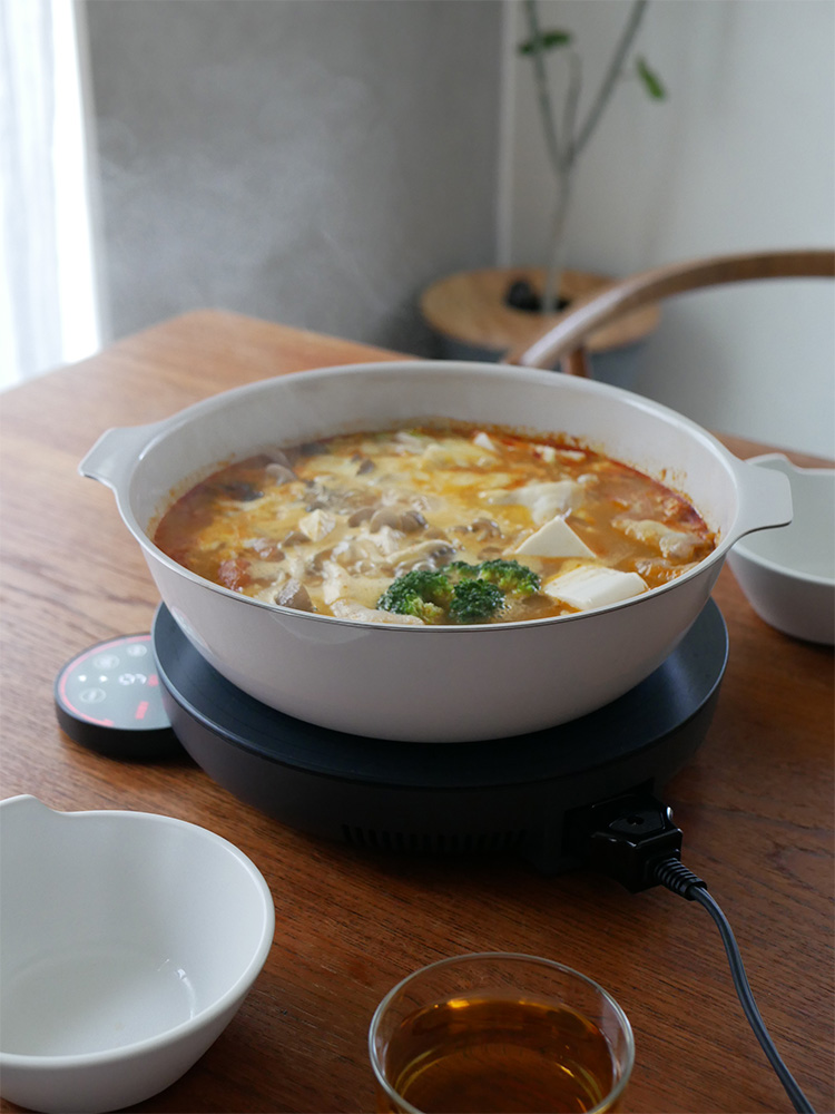 キントーの琺瑯×天然木IH卓上鍋KAKOMIとスチームプレートが調理台に置かれ、食材や食器とともに料理を準備しているキッチンシーン