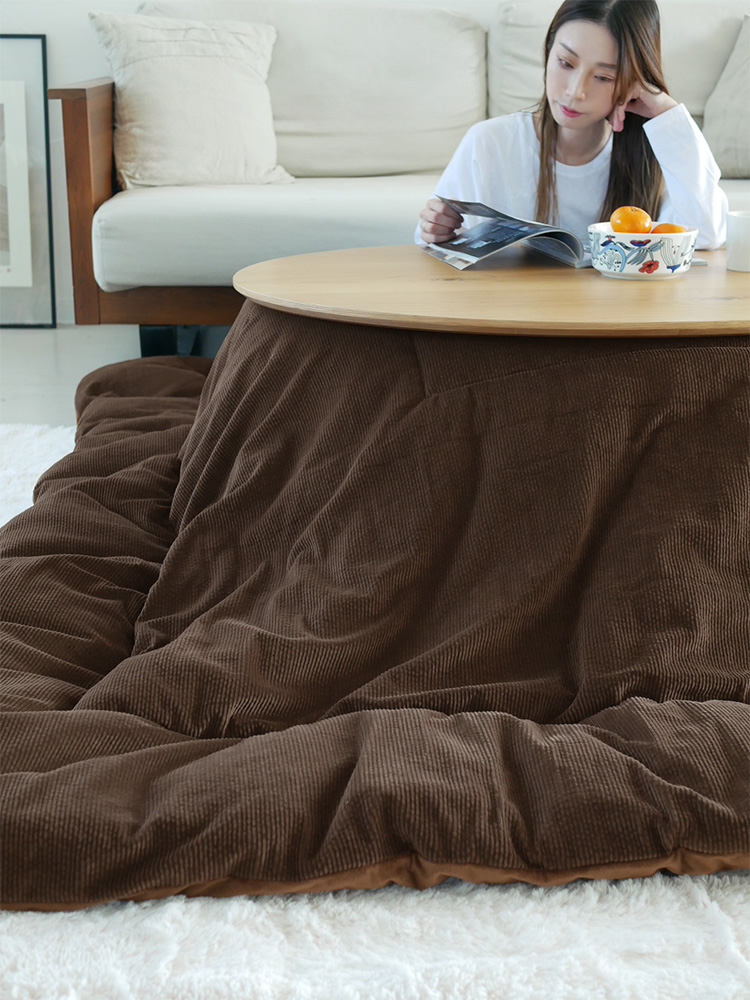 リバーシブルこたつ布団が敷かれたリビングルームで、こたつテーブルの上に食事が置かれ、クッションや観葉植物が配置されている様子