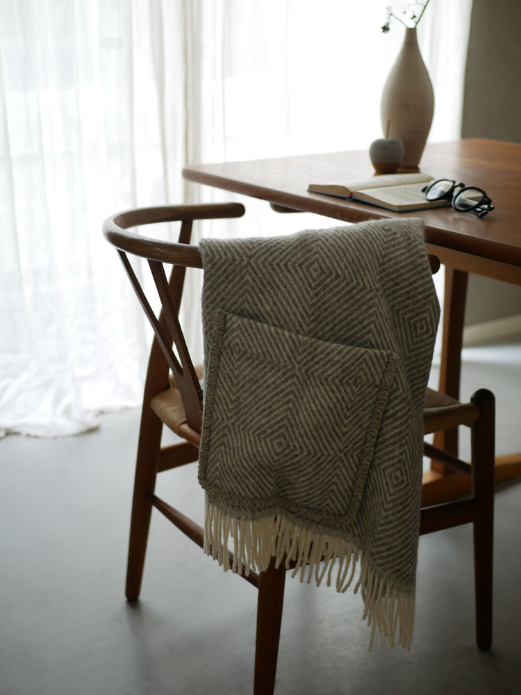 リトアニア製100％ウールのポケットショールMARIAが木製の椅子に優しく掛けられている様子