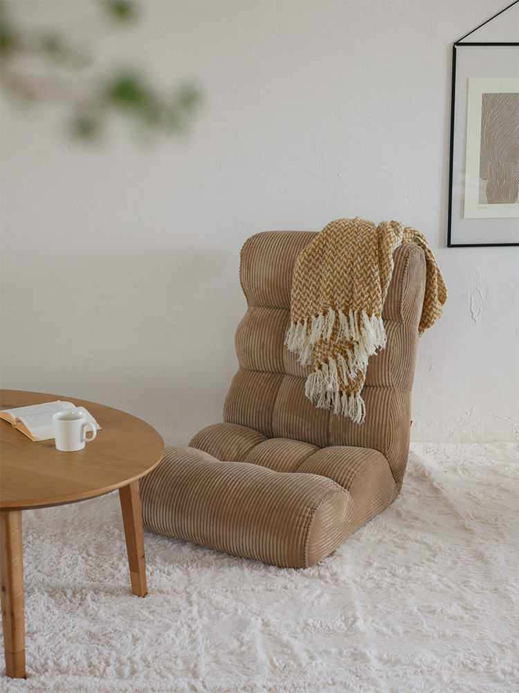 木製フローリングとカーペットが敷かれたリビングルームに置かれた、ブラウン色のウィッカー製クッション付き座椅子