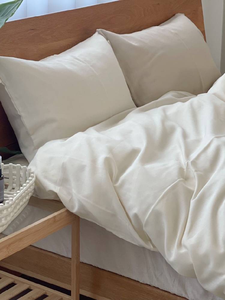 ココマニのオーガニックコットン布団カバーを使用したシングルサイズのベッドセット。枕やクッションが配置された温かみのある寝室風景。