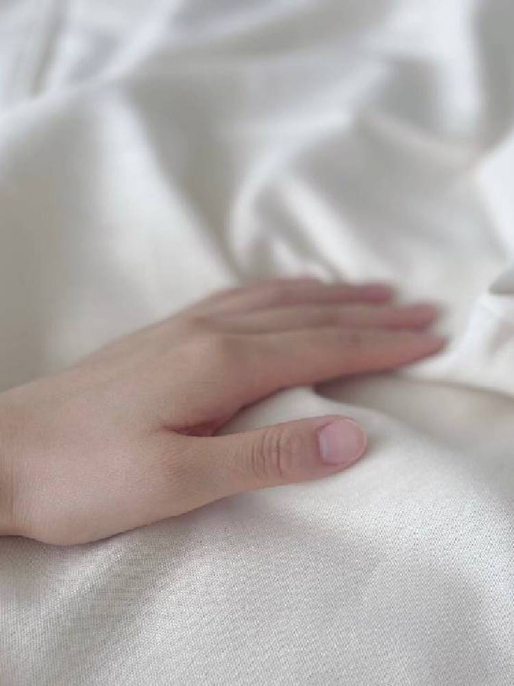 白いオーガニックコットン製布団カバーのリネン生地に指と爪が触れているクローズアップ写真