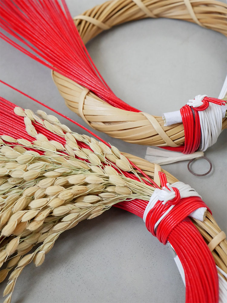 赤いリボンと縄を使い、竹や稲などの自然素材で作られた迎春ことほぎリースの籠型デザイン