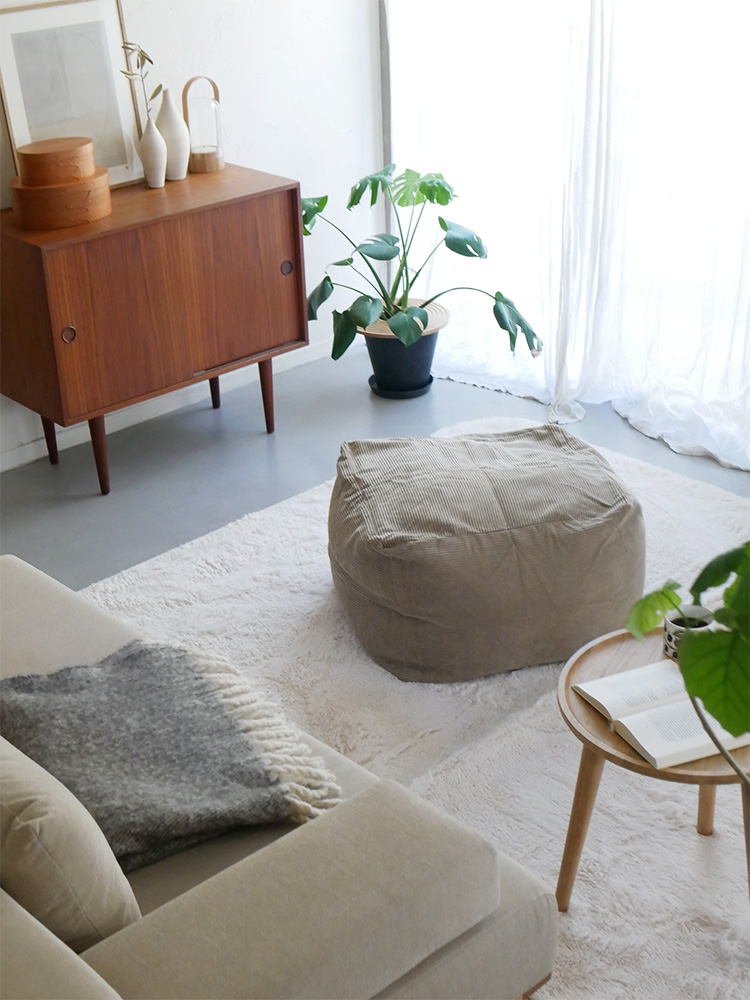 グレーのコーデュロイビーズクッションが配置されたリビングルームのインテリア。コーヒーテーブルと花鉢が調和する家具とフローリングが見える