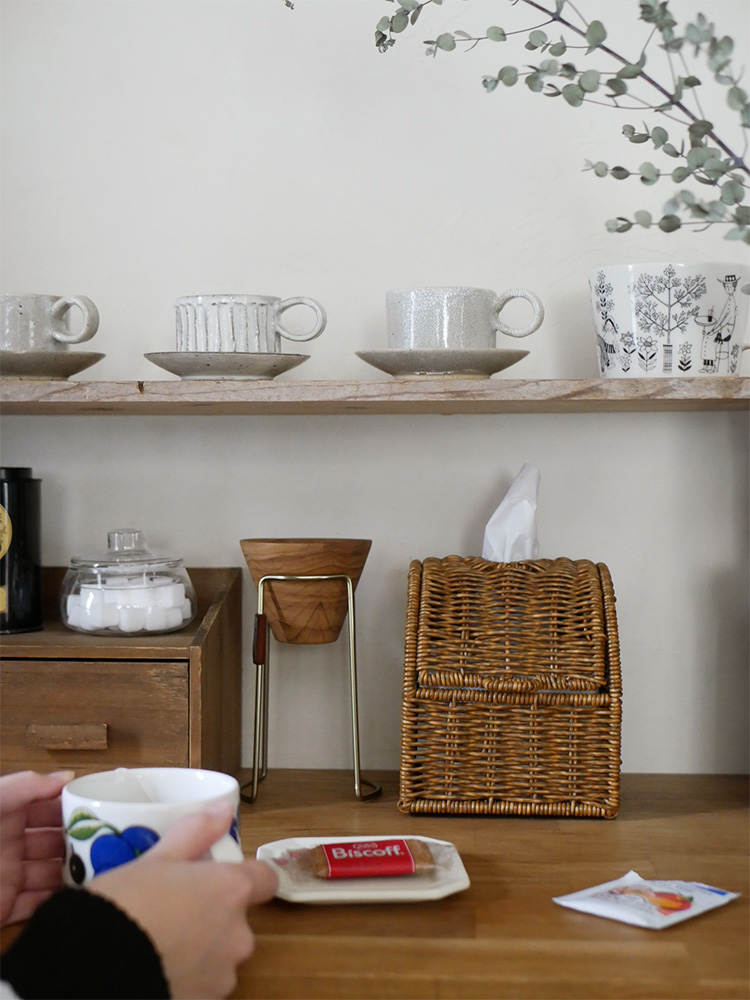 クレエのユティル洗えるコンパクトティッシュケースがテーブル上に配置されており、カップや花瓶などのテーブルウェアや家具が並んでいる様子。