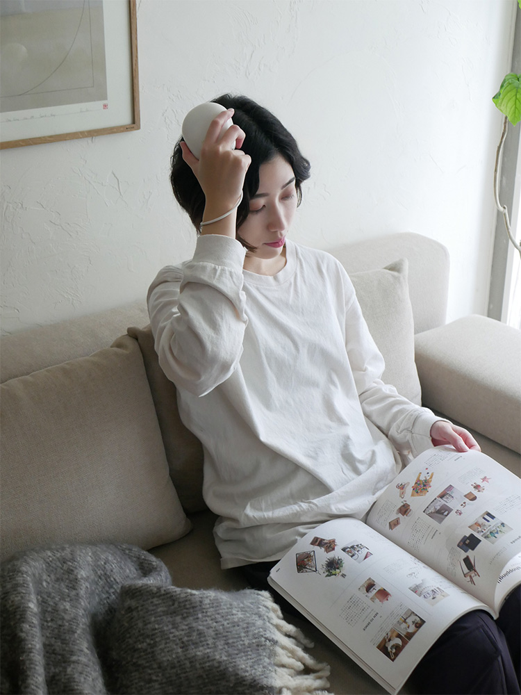 リビングルームのソファ上に置かれたフェスティノ充電式EMSヘッドスパと周囲のクッションや投げ枕が快適な空間を演出している様子