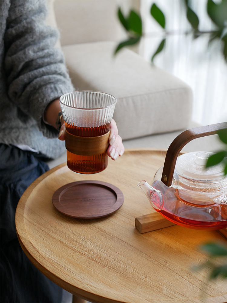 adepecheのnoonコレクション、ホウケイ酸ガラスとウォールナット製のティーポットとカップ、ソーサーがテーブルにセットされたティーウェア