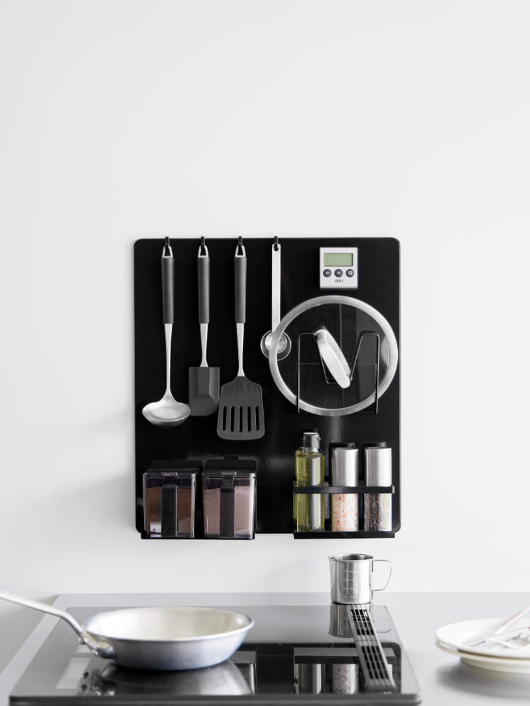 キッチンの壁に設置されたスチール製フィルムフックパネルに、食器や調理器具が整然と掛けられている様子