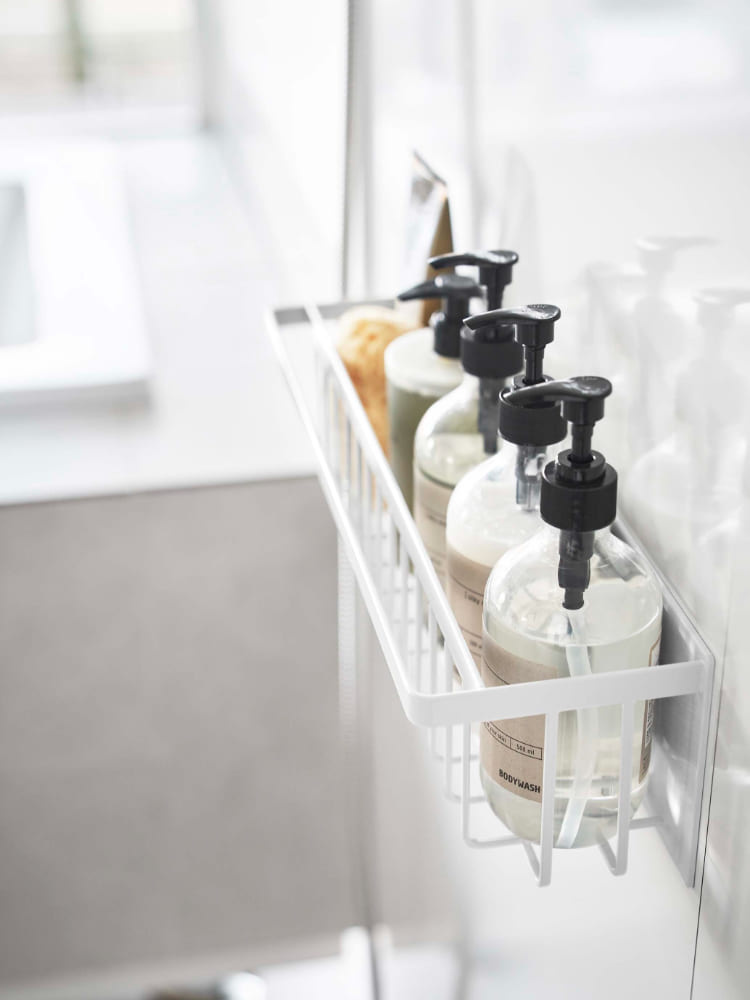 スチール製マグネットバスルームバスケットが洗面台横のスチール壁面に取り付けられ、ソープディスペンサーやボトルが整然と収納されている様子