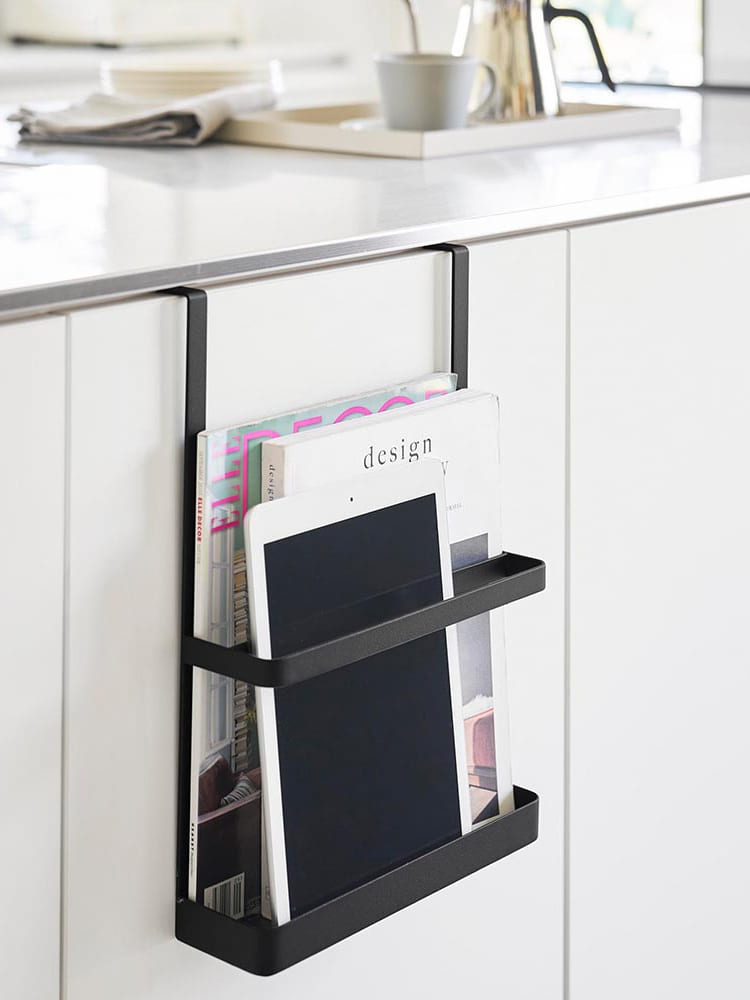 スチール製のタワー型引っ掛け宿題＆タブレットPCラックがキッチンの棚に取り付けられ、2つのフックとトレーが見える様子